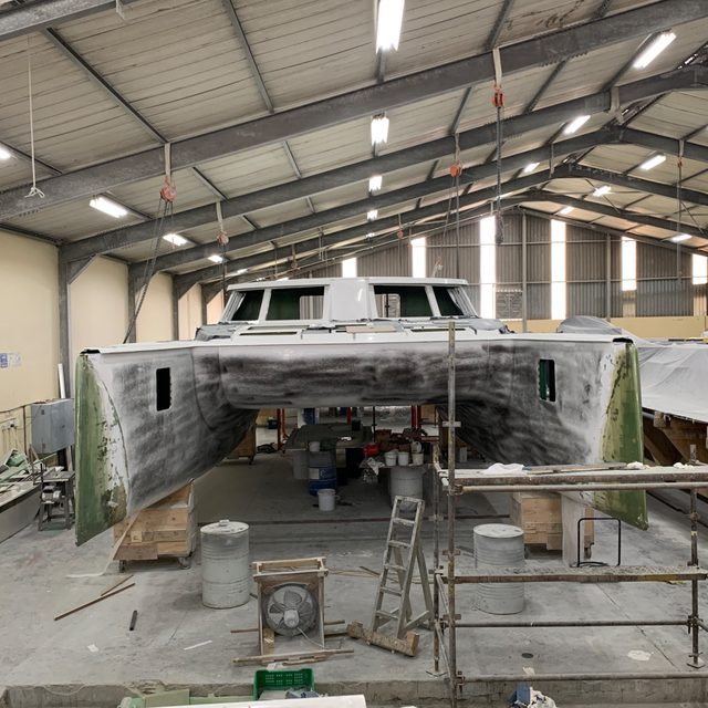 A catamaran inside a refit workshop with contractors at work